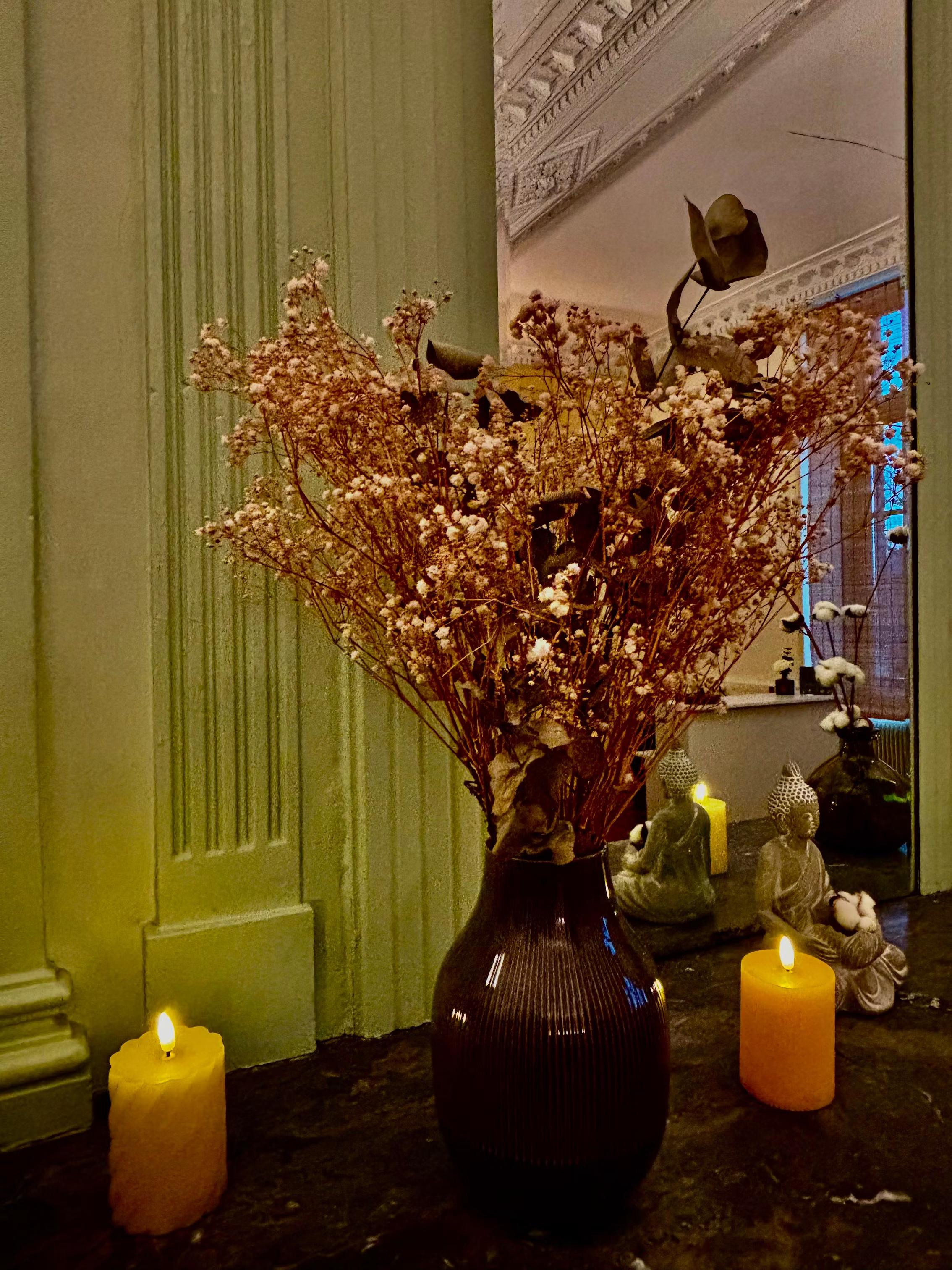 Bouquet de gypsophile séchée, bougies et statuette de Bouddha sur une cheminée devant un miroir, spa MCH