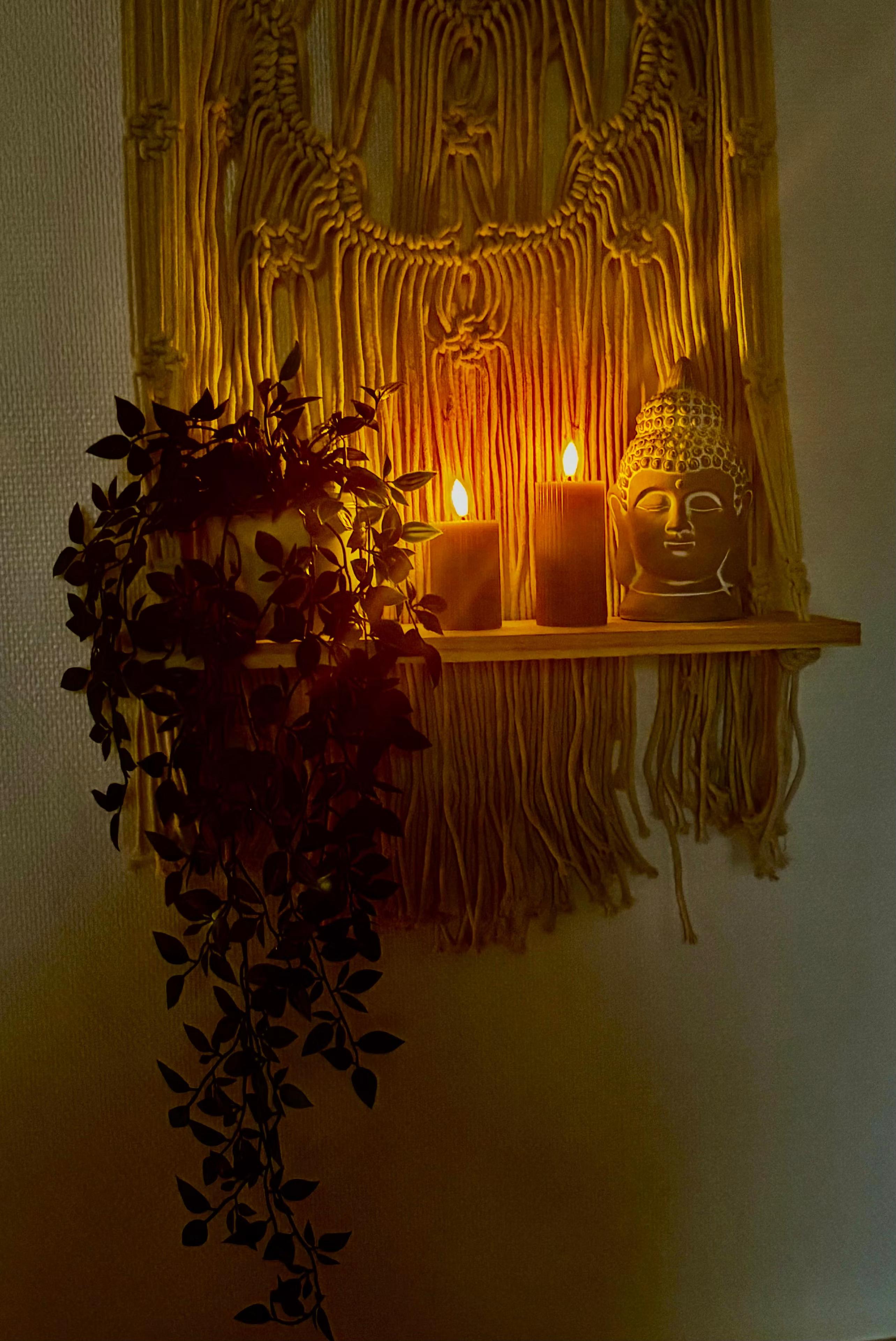 Étagère en macramé avec bougies allumées, tête de Bouddha et plante retombante, ambiance tamisée du spa MCH