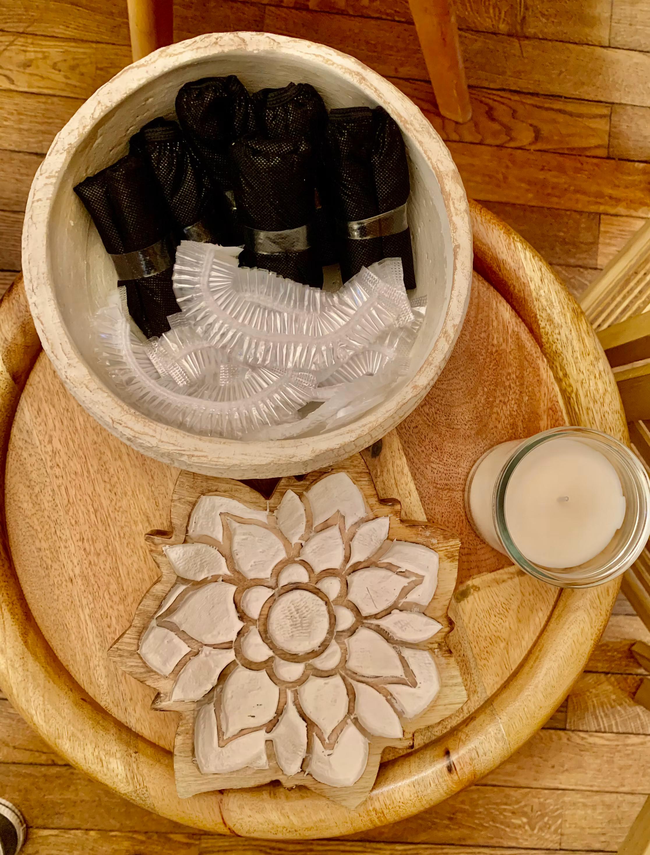 Sous-vêtements jetables et charlottes dans un bol, fleur sculptée en bois et bougie sur un plateau, spa MCH