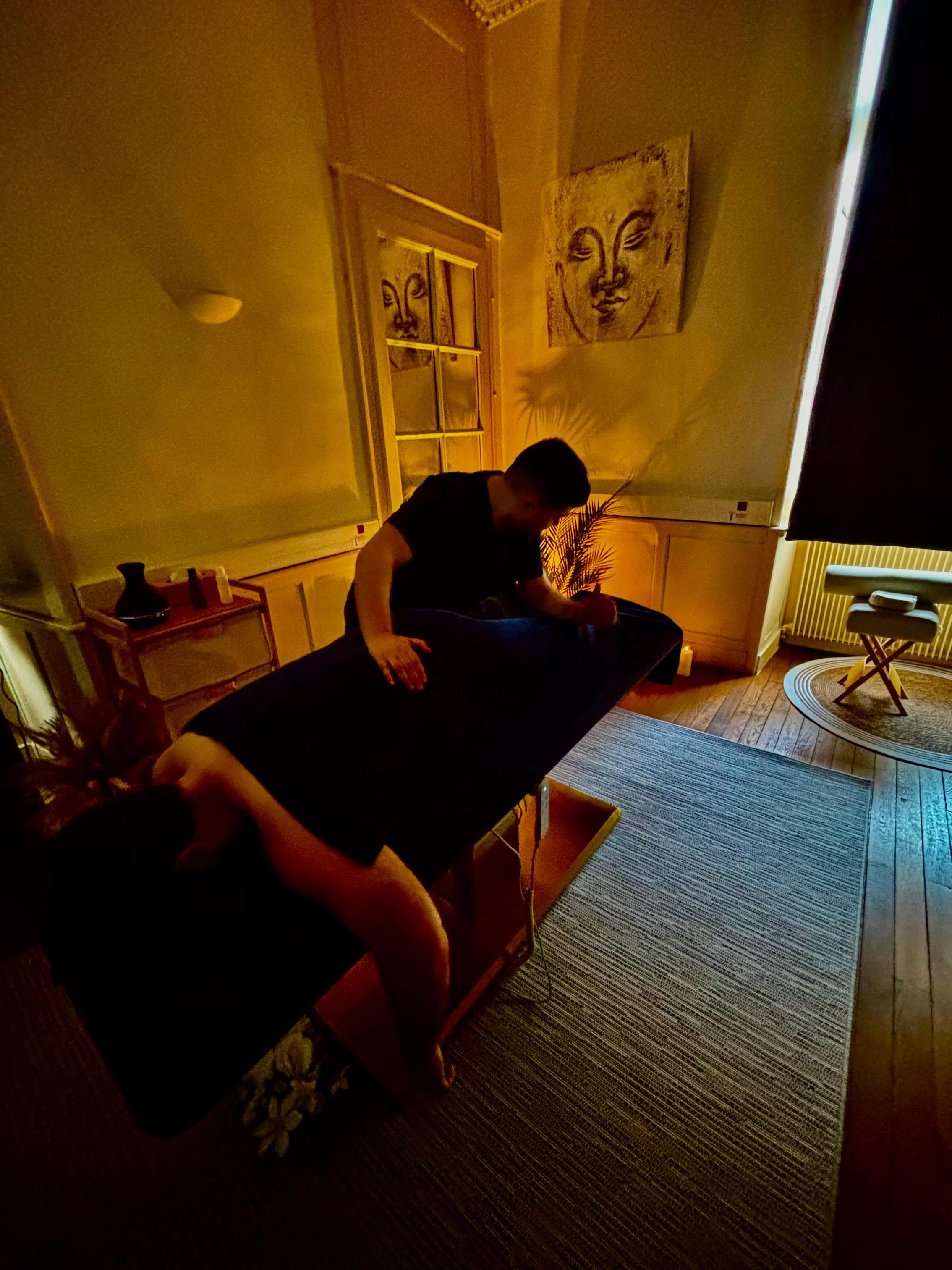 Praticien réalisant un massage du dos d’un client allongé sur une table de massage, dans une cabine de bien-être à l’éclairage tamisé et à la décoration zen.