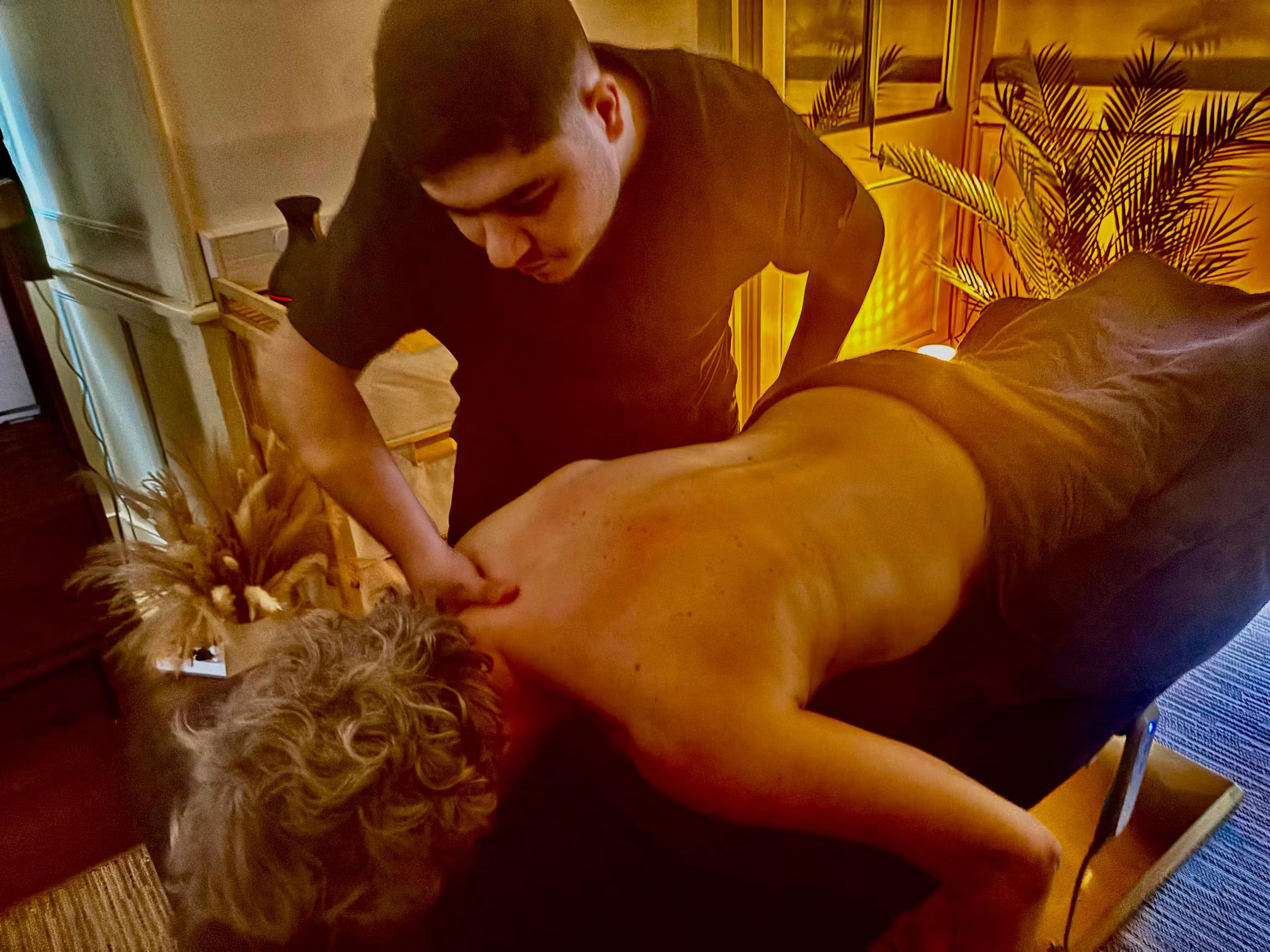 Praticien réalisant un massage du dos d’un client allongé sur une table de massage, dans une ambiance chaleureuse et tamisée.